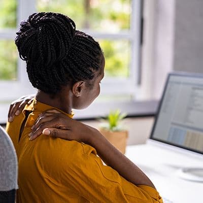 Büromitarbeiterin mit Nackenschmerzen als Beispiel für falsche Sitzhaltung am Arbeitsplatz